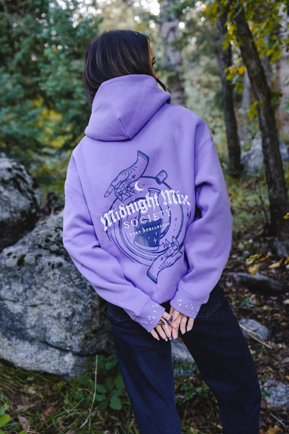 Back view of a model wearing a lavender Midnight Mix Society hoodie with her hands behind her.